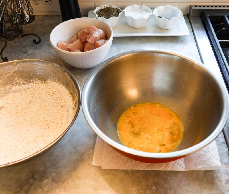 batter ingredients in bowl, beaten eggs in bowl, and cubed chicken