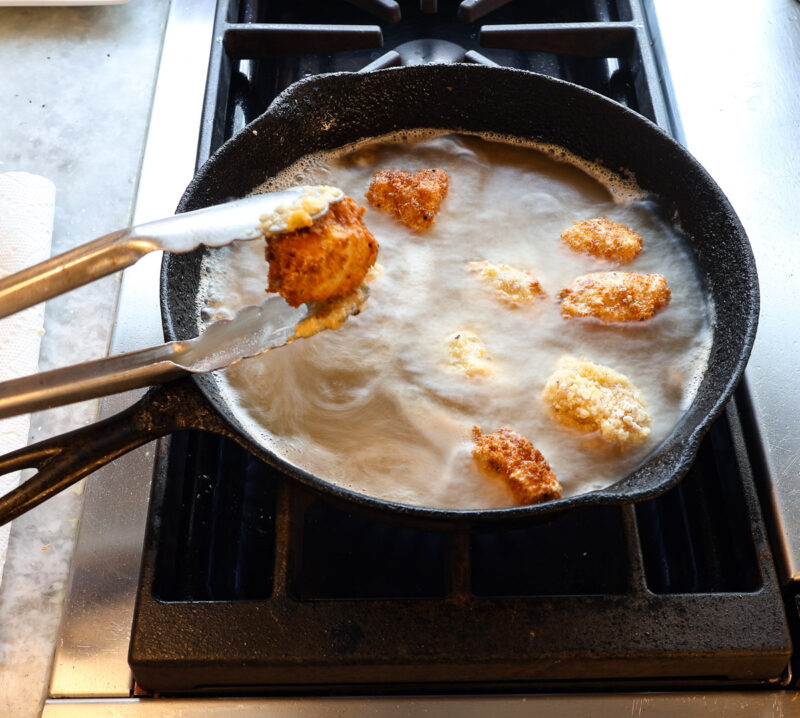 battered chicken cubes frying in cast iron skillet