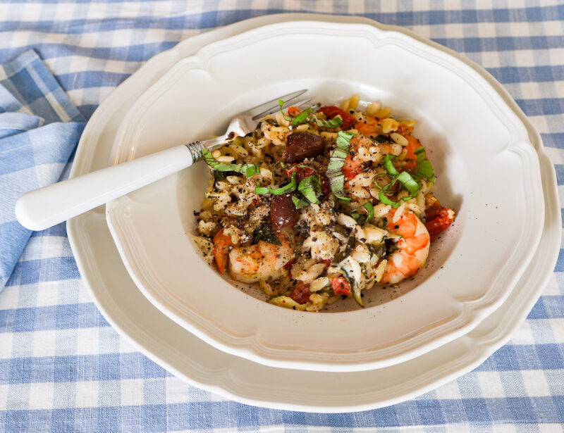 shrimp orzo with fresh vegetables and kalamata olives in a shallow bowl