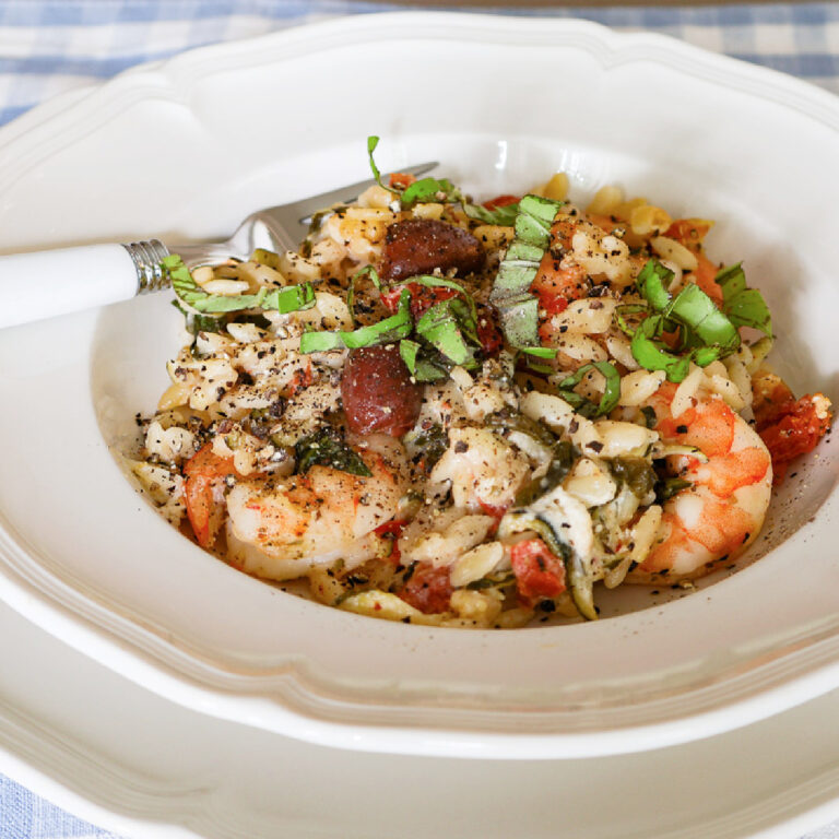 shrimp orzo with fresh vegetables and kalamata olives in a shallow bowl