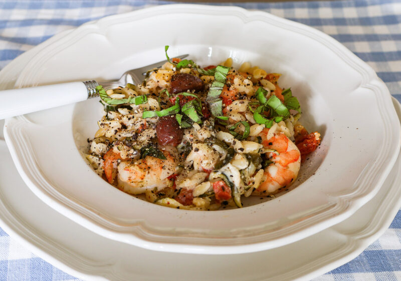 shrimp orzo with fresh vegetables and kalamata olives in a shallow bowl