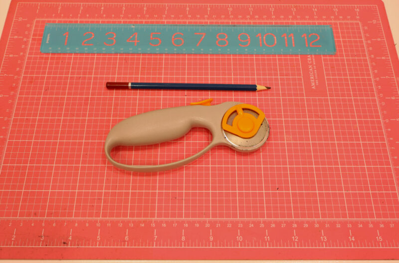 supplies for decorative file project - pink cutting mat, rotary cutter, ruler, and pencil