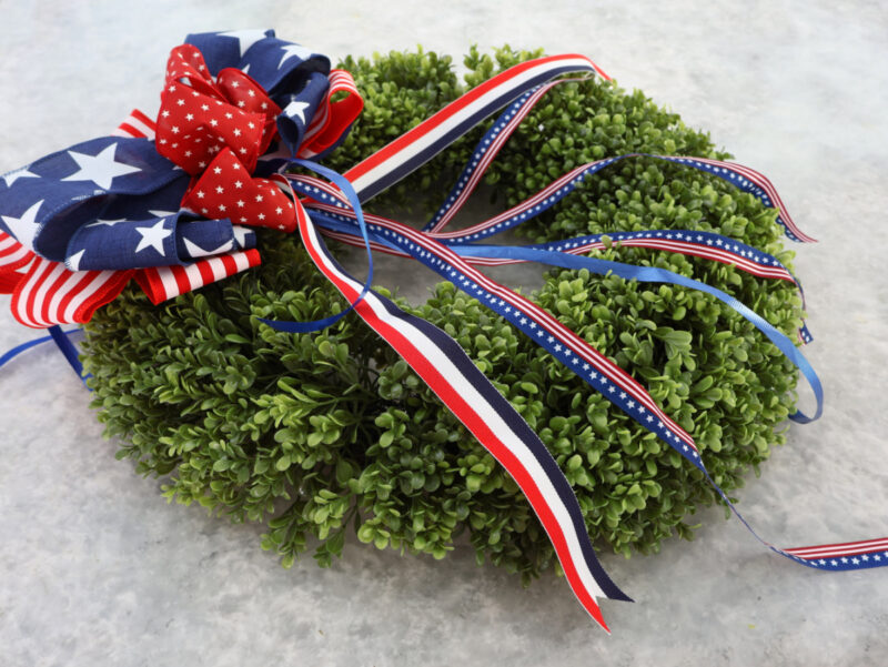faux boxwood wreath decorated with red, white, and blue bow and ribbon