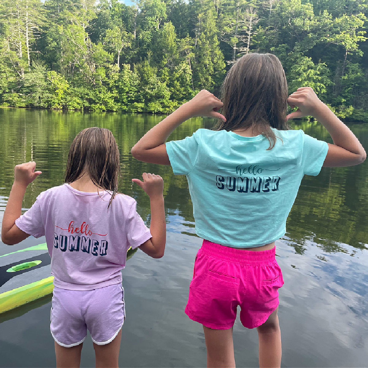 two girls at a lake pointing to their painted and stenciled t-shirts