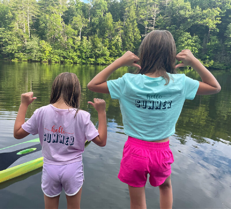 two girls at a lake pointing to their painted and stenciled t-shirts