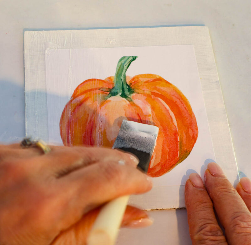 adding mod podge to orange painted decorative pumpkin drawing
