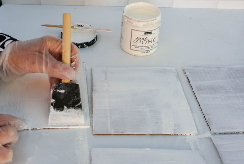 adding white paint to square cardboard tiles