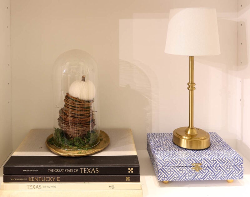 stacked twig nests inside cloche on metallic clay tray on bookshelf.